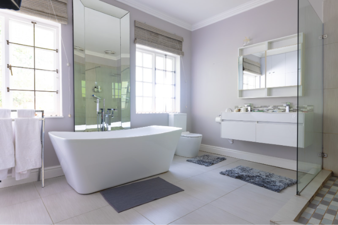 Bright modern bathroom with a freestanding white bathtub, glass shower, floating vanity, large mirrors, and light tile flooring.